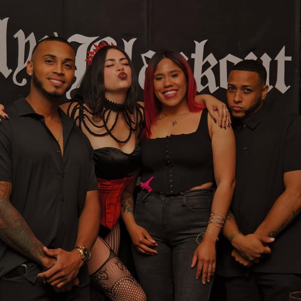 Four young adults, two men and two women, pose together in front of a dark background.