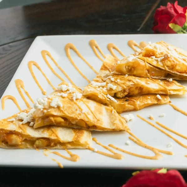 Golden quesadilla triangles with melted cheese, drizzled with sauce and crumbled feta on a white plate.