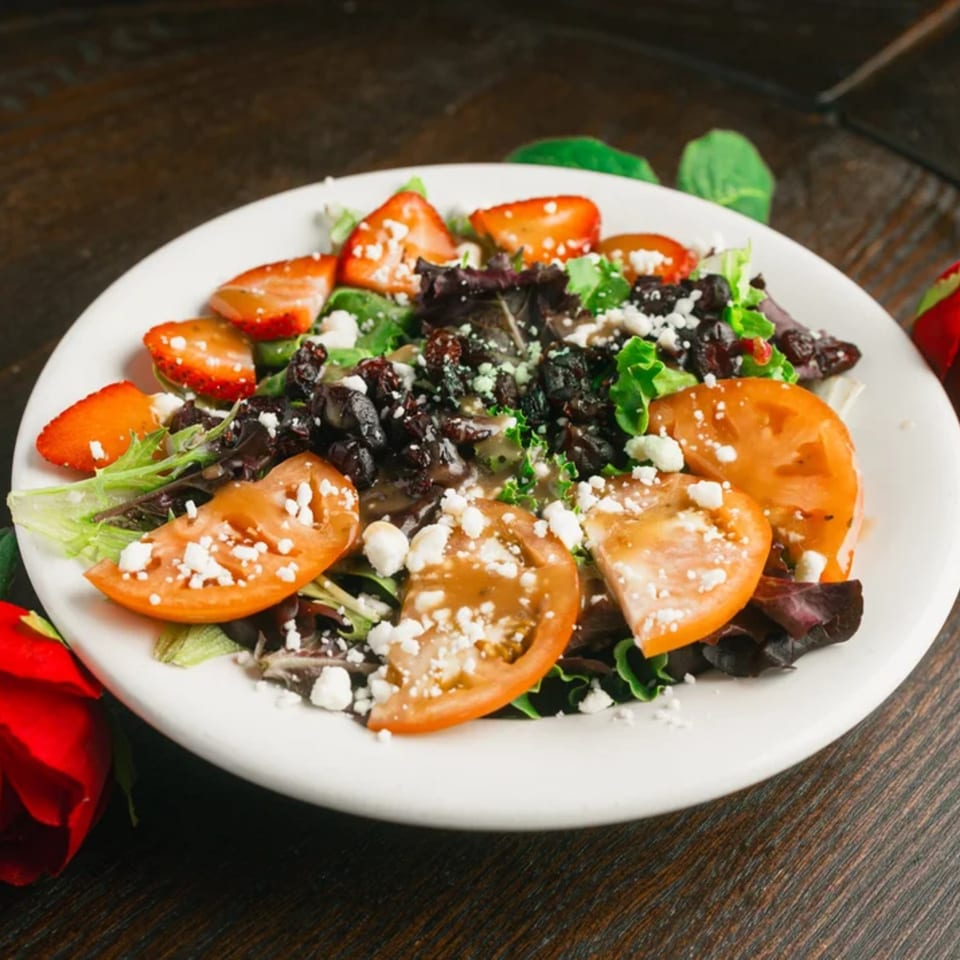 Colorful salad with mixed greens, sliced strawberries, tomatoes, dried cranberries, and crumbled cheese.