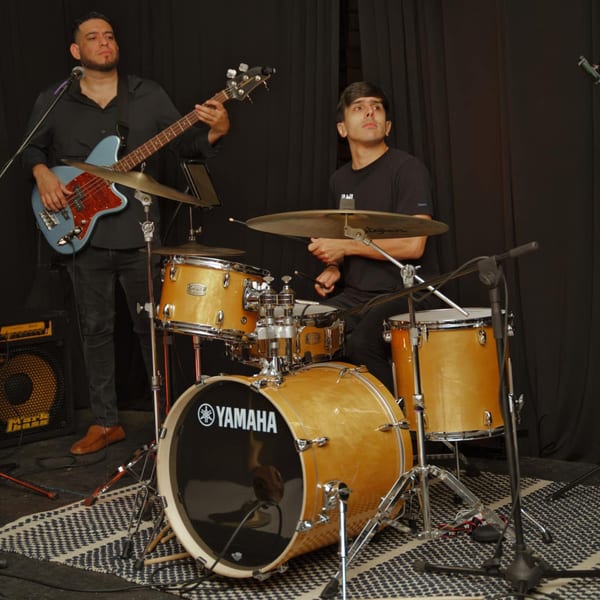 Two musicians, a bassist and a drummer, performing live on stage with their instruments.
