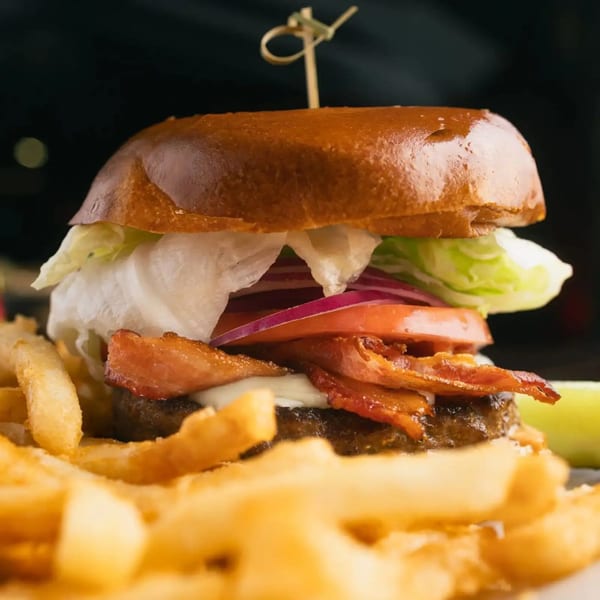 A bacon cheeseburger with lettuce, tomato, and onion, served with a side of golden fries.