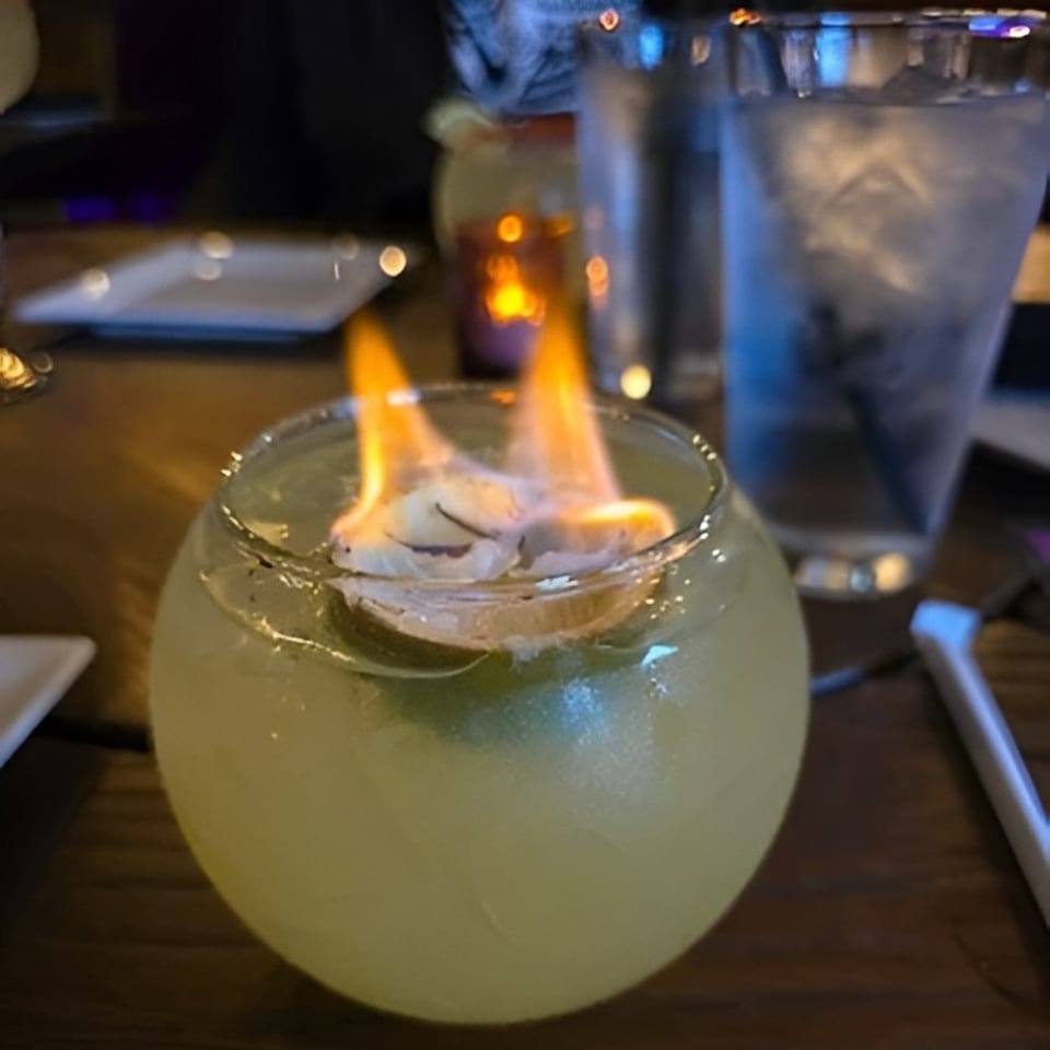 A flaming cocktail in a round glass, with a slice of lime and fire on top.