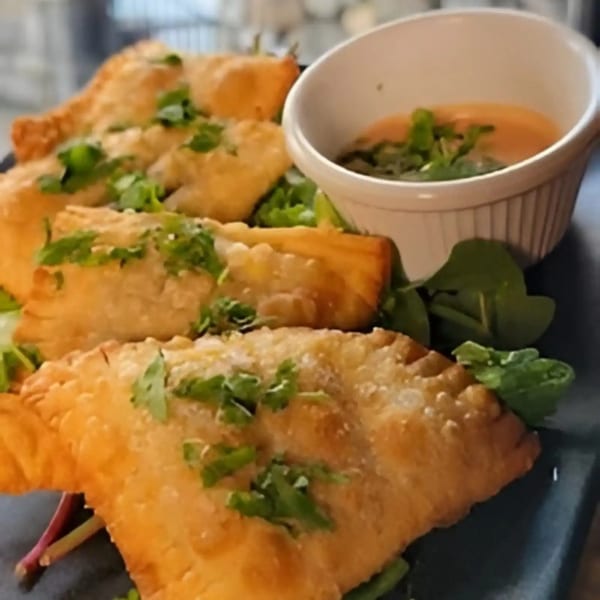 Golden-fried empanadas with fresh cilantro and a side of dipping sauce on a dark plate.