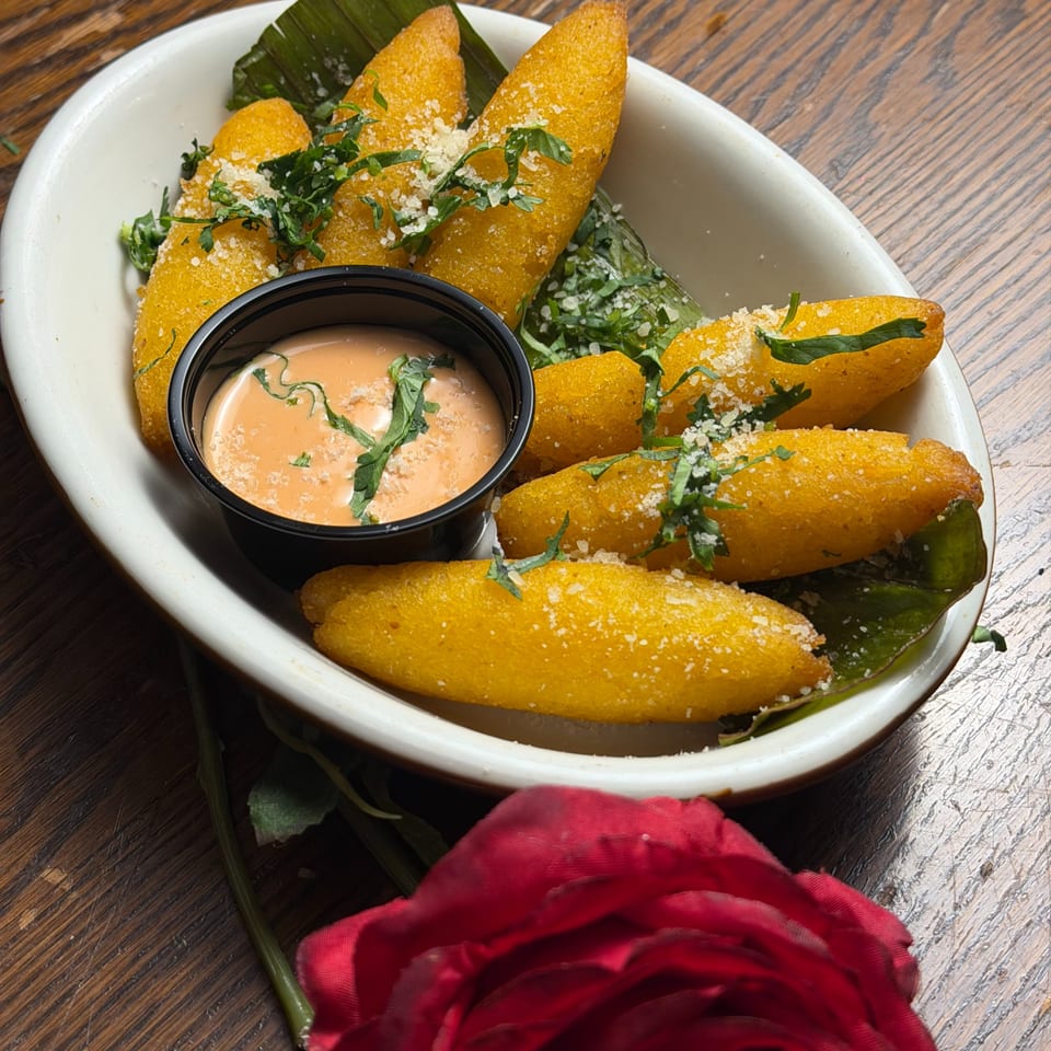 Golden fried plantain fritters with cheese and herbs, served with a dipping sauce and a red rose.
