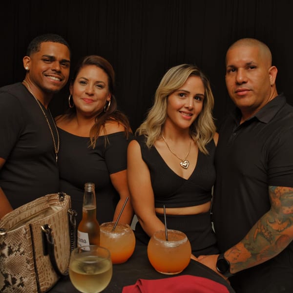 Two couples smiling at the camera with drinks and a purse on a table in front of them.